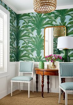 a dining room with green palm wallpaper and blue upholstered chairs in front of a round wooden table