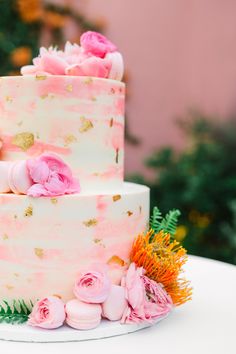 a three tiered cake with pink flowers and gold flecks on the top