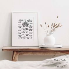 a white vase sitting on top of a wooden table next to a framed crown print