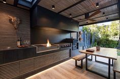 an outdoor kitchen with wood flooring and black walls, along with a fire place in the center