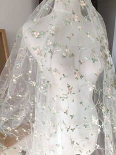 a white veil with flowers on it is sitting on a mannequin's head