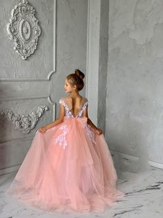 Introducing the Malita Luxury Couture Flower Girl Dress, a masterpiece crafted for those moments that will be cherished forever. This exquisite dress features a satiny bodice that gleams with elegance, paired with a daring plunging V neckline at the back, adding a touch of sophistication and charm. The highlight is a delicate bow that sits gracefully at the back, symbolizing purity and innocence. Cascading to the floor, the full-length tulle skirt creates an ethereal silhouette, making it perfec