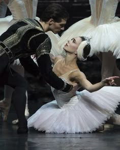 two ballerinas in white tutus and black leotards, one is holding the other's leg