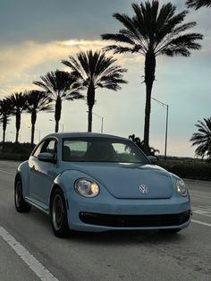 a blue car driving down the road next to palm trees