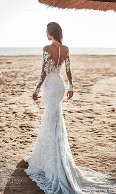 a woman standing on top of a sandy beach wearing a white wedding dress with long sleeves