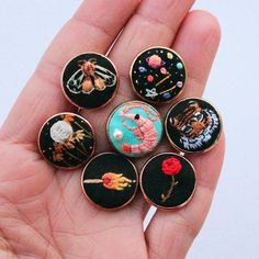 a person is holding six small buttons in their hand, each with different designs on them