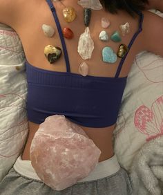 a woman laying in bed with her back to the camera, covered by stones and crystals