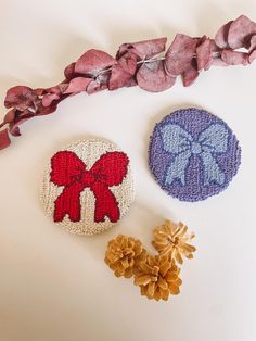 two decorative buttons with bows on them next to some pine cones and dried flowers in the foreground