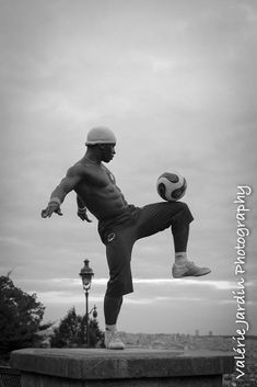 a man kicking a soccer ball on top of a cement wall near a lamp post