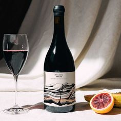 a bottle of wine next to a glass and grapefruit on a white table cloth