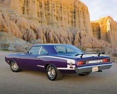 a purple car is parked in front of some mountains and rocks, with a rock formation behind it