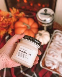 a person holding a jar of pumpkin art next to some other items on a table