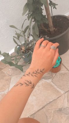 a woman's hand with a ring on her left wrist next to a potted plant