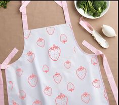 an apron with strawberries on it sitting next to some vegetables and utensils