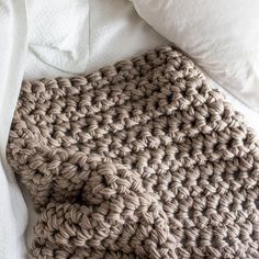 a crocheted blanket laying on top of a bed next to pillows