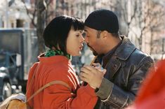 a man and woman standing next to each other in front of a tree filled with leaves