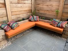 an orange bench sitting next to a wooden fence with pillows on it's back