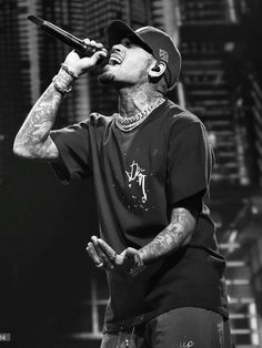 a man with tattoos on his arm holding a microphone in front of him and looking up at the sky