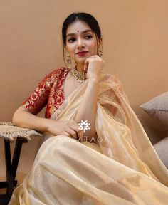 a woman sitting on top of a couch wearing a white and red sari with gold accents