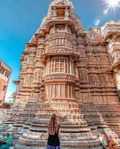 a woman standing in front of an intricately carved building with sun shining through the sky