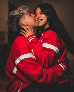 two people are kissing each other while sitting on a couch and one person is wearing a red jacket