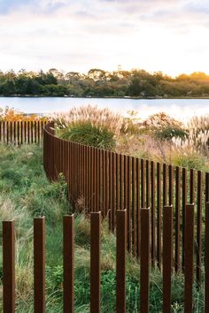 a wooden fence next to a body of water with tall grass in the foreground