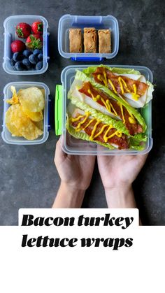 a person holding a plastic container filled with food next to some fruit and crackers