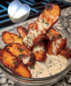 a glass bowl filled with chicken wings covered in gravy and parmesan cheese