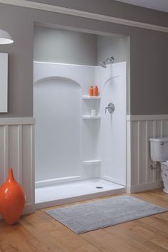 an orange vase is sitting on the floor in front of a white bathtub and shower