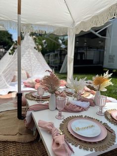 a table set up with plates and pink napkins under an umbrella for a party