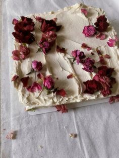 a cake with white frosting and red flowers on it sitting on a tablecloth