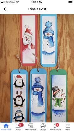 four tags with snowmen and penguins painted on them, hanging from the side of a wooden table