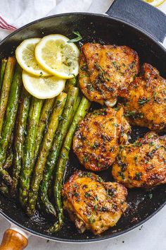 chicken and asparagus in a skillet with lemon wedges