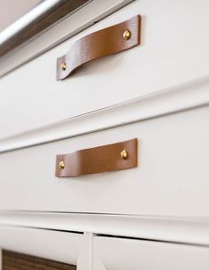 a white dresser with brown leather handles