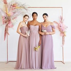 three women in long dresses standing next to each other with flowers and feathers on them