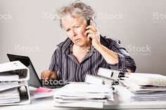 an old woman is sitting at her desk talking on the phone and holding a laptop computer