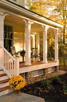 a porch with white pillars and yellow flowers on the front steps next to an outdoor dining area