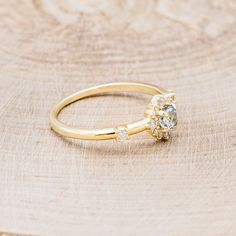 a yellow gold ring with an aqua blue diamond and white topaz stones sits on a piece of wood