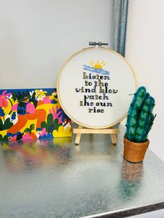 there is a cross - stitch pattern on the table next to a potted cactus