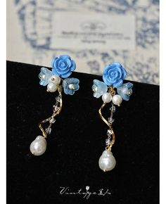 two blue roses and pearls are attached to the back of some ear pins on a black surface