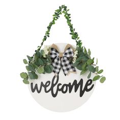 a welcome sign hanging from the side of a white wall with greenery and bows