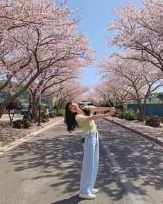 a woman standing in the middle of an empty road with cherry trees lining both sides