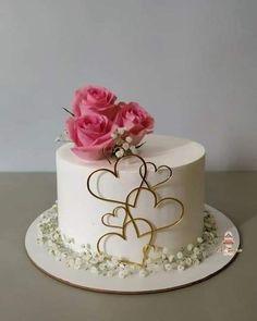 there is a white cake with pink roses on the top and two hearts on the bottom