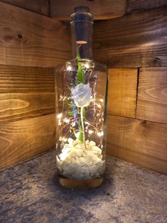 a glass vase filled with white rocks and flowers on top of a counter next to wooden planks