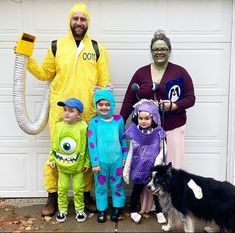 three adults and two children in costumes standing next to a garage door with a dog