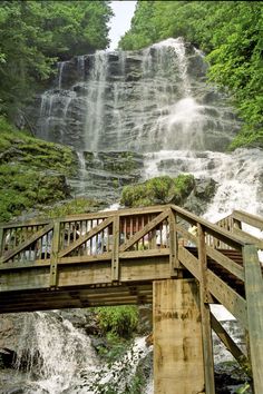 a wooden bridge over a small waterfall with people standing on the top and below it