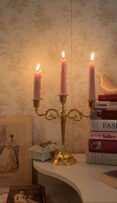 three candles are lit on a table with books in front of it and a wallpapered background