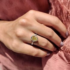 a woman's hand with a yellow diamond ring on her left hand and a pink dress