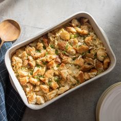 a casserole dish with chicken and bread in it next to a wooden spoon