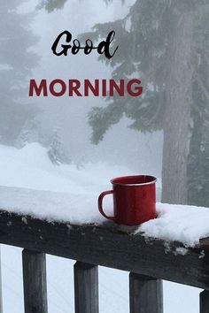 a red coffee cup sitting on top of a wooden rail next to snow covered trees